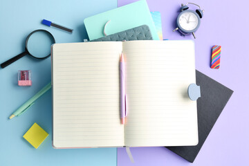 Composition with blank open notebook, different stationery and alarm clock on color background