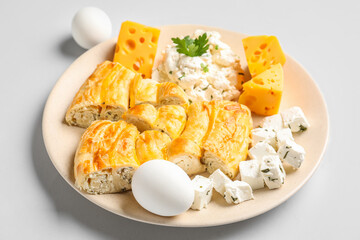 Plate with pieces of delicious cheese pie and ingredients on grey background