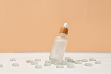 Bottle of serum and glass stones on light wooden table against color background