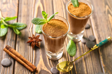 Shots of delicious chocolate pudding with cinnamon and mint on wooden table