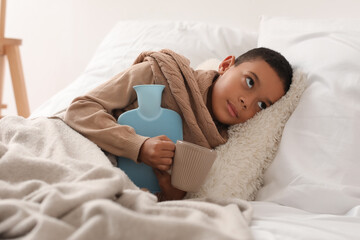 Ill African-American boy with hot water bottle in bedroom