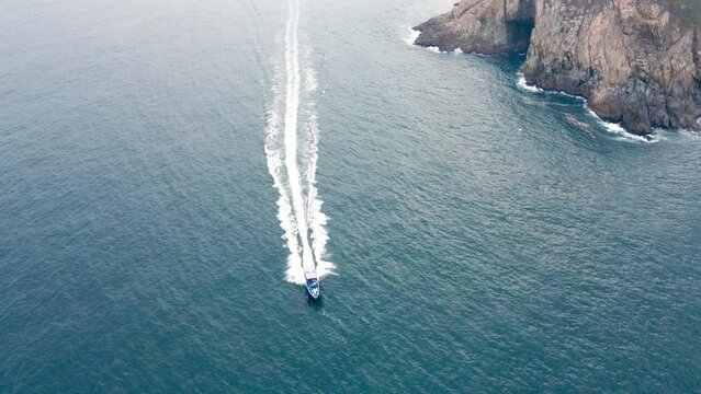 Aerial view following a moving boat. Hong Kong coastline. Drone view of ocean waves. Cliffs. 