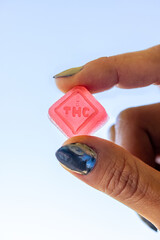 Female model holding a THC gummy between her fingers with sky in the background