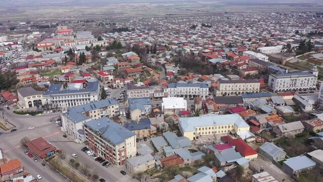 Scenic view from drone of central area of Telavi city overlooking large avenue with modern buildings surrounded by old small houses on spring day, Georgia