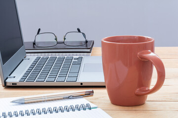 Workplace. A laptop, notebooks with a pen, glasses and a cup of coffee on the desktop