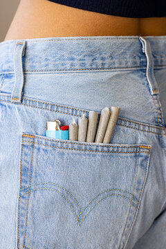 A collection of prerolls and lighter in the back pocket of a female model wearing jean shorts. 