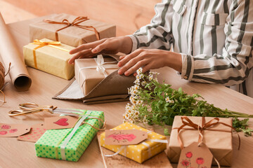 Fototapeta na wymiar Woman wrapping gift box for International Women's Day at wooden table, closeup
