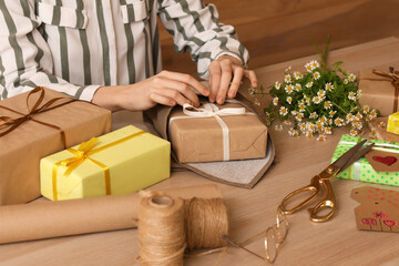 Woman wrapping gift box for International Women's Day at wooden table, closeup