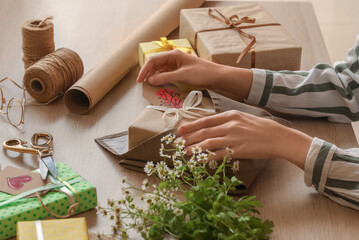 Naklejka na ściany i meble Woman wrapping gift box for International Women's Day at wooden table, closeup