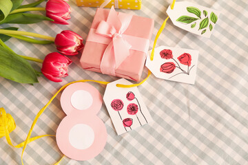 Gift box with paper tags, figure and tulips for International Women's Day on checkered fabric background