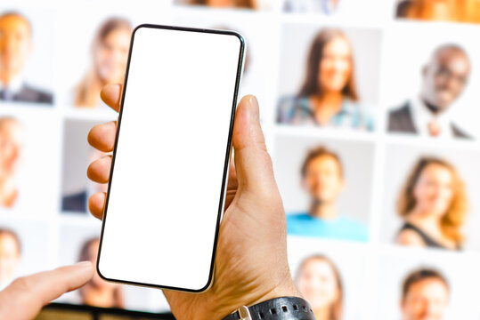 Male holds mockup white blank screen mobile phone to create something.Man using Artificial software on mobile phone to create realistic generated image.Blurred PC monitor collage portrait background.