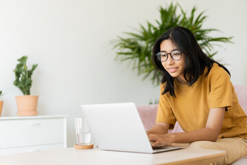 Asian woman wear glasses typing work on laptop computer happy at home - 566146971