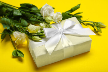 Beautiful gift box with eustoma flowers on yellow background, closeup. Women's Day celebration