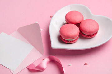 Heart-shaped plate with tasty macaroons and envelope on pink background. Valentine's Day celebration