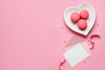 Heart-shaped plate with tasty macaroons and envelope on pink background. Valentine's Day celebration