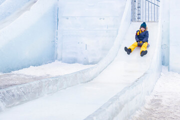  happy boy slides down an ice slide in winter outside