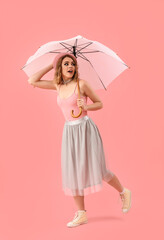 Beautiful young woman with umbrella on pink background