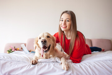 young girl lies on a bed with golden retriever dog and smiles, a woman with a pet rest at home