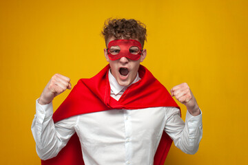 guy in a superman costume screams and rejoices in victory on a yellow background, a man is a super hero