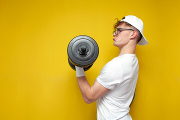 confident guy student lifts heavy dumbbells and trains on a yellow background