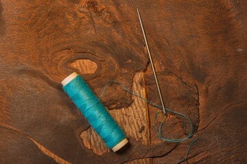 A spool of thread and a needle lie on a dark wooden background. Clipart photo