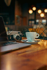 Photo of a cup of coffee with late art drawn on it, laptop notes and a vintage camera on the table next to the coffee cup