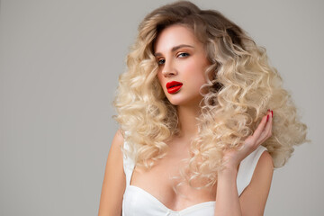 A beautiful curly blonde with long hair raises and shows her hair with her hand. Makeup with red lips