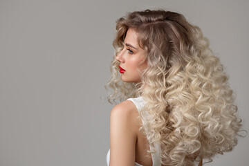 Curly fashion blonde woman with long hair and makeup. Back view. Grey background