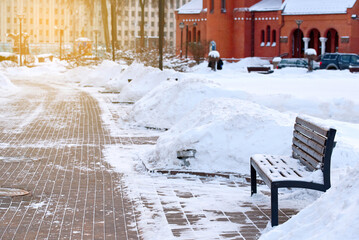 Bench among snowdrifts in the city after snow storm. Wooden bench in park, bench cleared of snow. Snow drift on sidewalk. Bench in the park after heavy snowfal