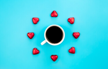 Chocolate sweets in the form of hearts and a cup of coffee on a blue background.