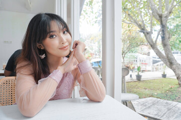 A smiling Asian woman wearing pink dress while sitting near window