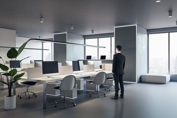Fototapeta na wymiar Thoughtful european businessman standing in modern concrete coworking office interior with window and city view, daylight, furniture and equipment.