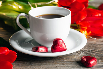 Composition with a cup of coffee, heart-shaped sweets and red flowers close-up.