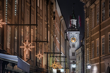 Obraz premium Salzburg, Austria - Illuminated clock tower of the former Old Town Hall at Christmas decorated Grain Lane (Getreidegasse) famous shopping narrow street in historic Altstadt by night