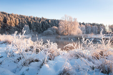 First month of spring, march. Beautiful landscape of nature in early frozen morning. All nature in hoarfrost. Sunbeams illuminate the edge of the forest. Over river are light mist. 
