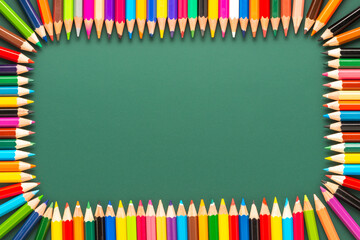 wreath of multicolored pencils on green chalkboard background, top view, copy space, back to school concept