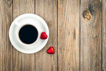 A cup of coffee and heart-shaped chocolates on a wooden background, top view.