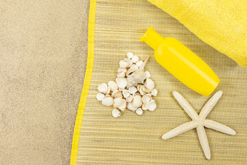 White heart made of seashells with starfish and yellow bottle of sunscreen and towel on straw lounger on sand. Concept vacation, Valentine's Day, holiday on beach. Copy space