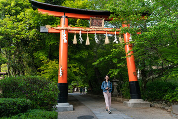 full length of asian Japanese woman visitor walking through a giant red torii entrance gate on stone pavement while visiting ujigami jinja in uji Kyoto japan on a sunny day