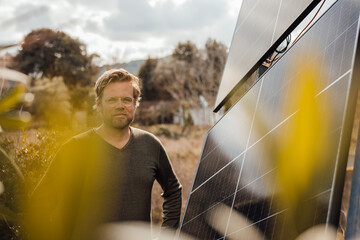 Smiling mature man wearing eyeglasses standing by solar panels