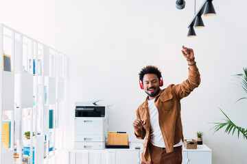 Carefree businessman wearing wireless headphones dancing in office