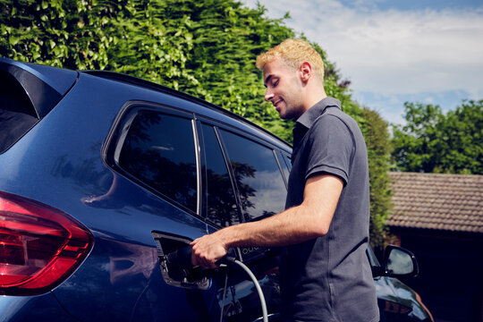 Smiling man plugging charger in electric car