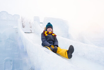Fototapeta na wymiar happy boy slides down an ice slide in winter outside