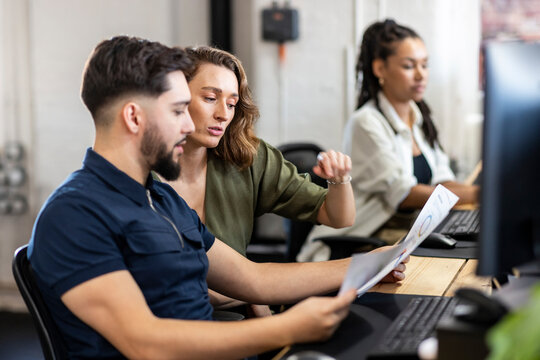 Businesswoman with coworker explaining charts at desktop in office