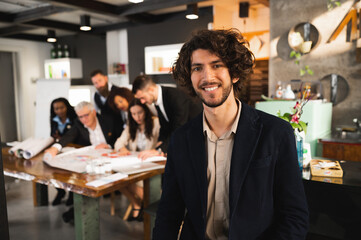Young hipster man posing at camera smiling. Multiracial Businesspeople working at workplace in background