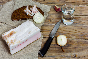 Rustic salted bacon with black bread and a glass of vodka on a wooden surface
