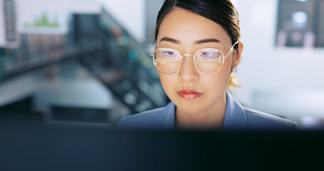 Face, glasses and management with a business asian woman at work on a computer in her office. Data, reading and email with a young female employee working on a report using a desktop for research