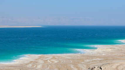 Landscape view of the Dead Sea with patterned salt deposit coastline and turquoise water in Jordan Rift Valley, Middle East