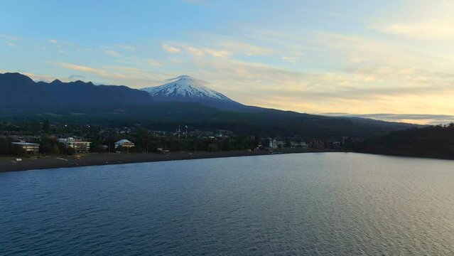 Aerial orbiting shot over Villarrica lake. Villarrica volcano in the distance and Pucon Chile town in foreground.