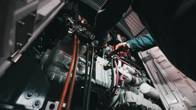 mechanic working on a reefer trailer, inserting an cordless electric screwdrive. Repair truck and trailer shop - low angle shot